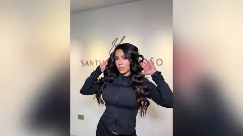 Confident woman in a black athletic zip-up jacket posing against a minimalist studio wall.
