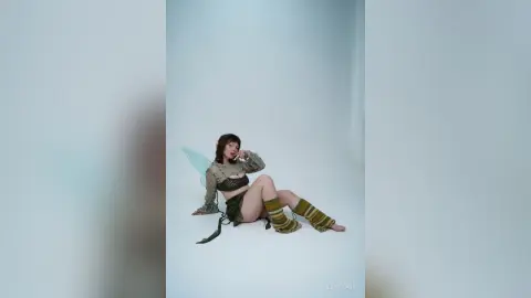 Woman in olive green fairy costume with translucent wings sitting on a white studio floor.