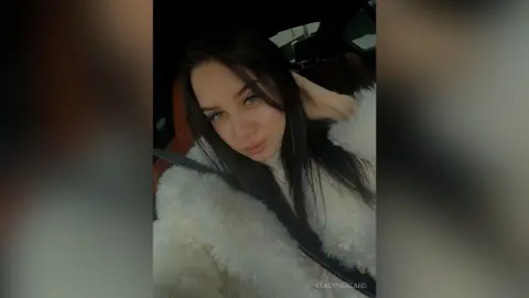 StacyHarland — StacyHarland poses in a car wearing a white furry coat with her long dark hair falling over her shoulders.