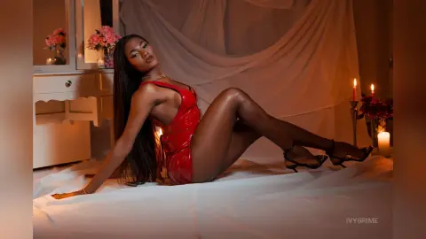 Elegant woman in a red satin dress reclining on a white bed in a romantic, candlelit bedroom setting.