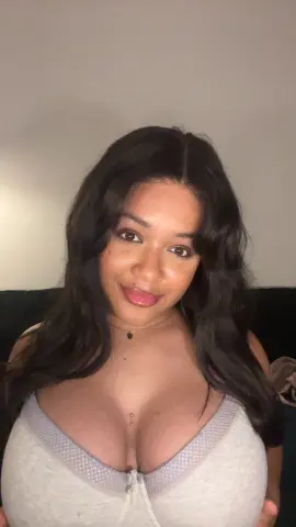 Hazelvalentine smiles, showing her long dark hair and cleavage while wearing a white zip-up top and a black necklace.
