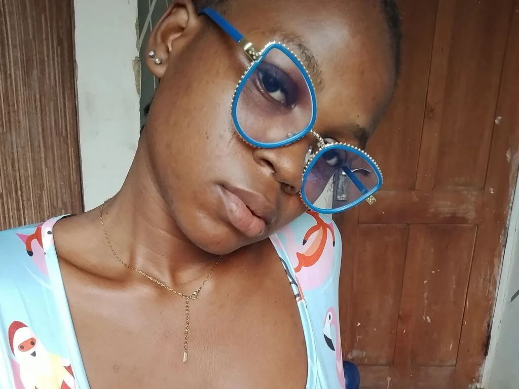 DahNorah wears blue glasses and a light blue patterned tank top while looking into the camera.