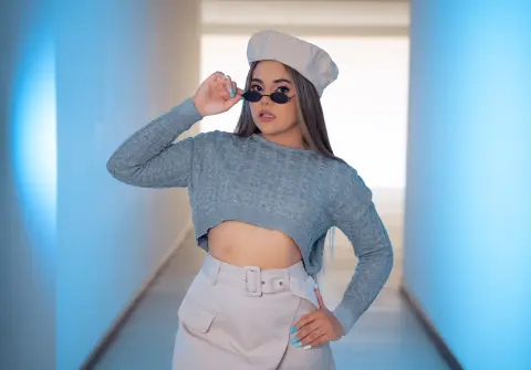 Stylish woman in a grey sweater and white beret posing in a bright blue hallway with a chic aesthetic.
