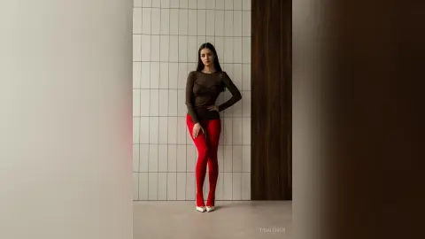 Elegant woman in a black long-sleeve top and red leggings posing against a white tiled wall in a modern setting.