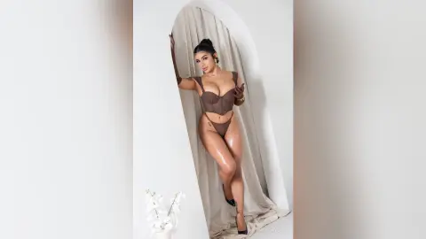 Glamorous woman in a brown bodysuit posing in an elegant arched doorway setting.