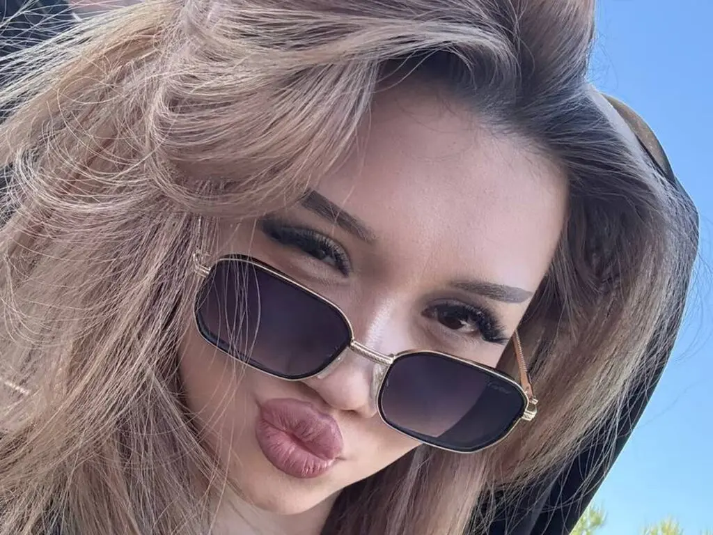 GailMayette pouts her lips while wearing dark sunglasses and letting her long blonde hair fall over her shoulders.