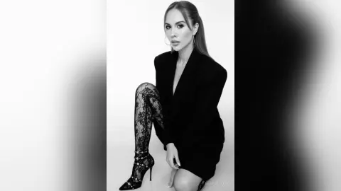 Elegant woman in a black blazer and lace tights posing against a white background in a chic studio setting.