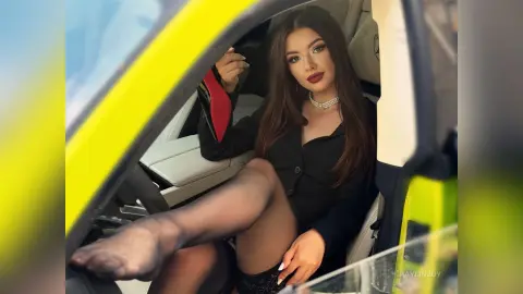 Glamorous woman in a black dress and sheer tights sitting in a luxury yellow supercar.