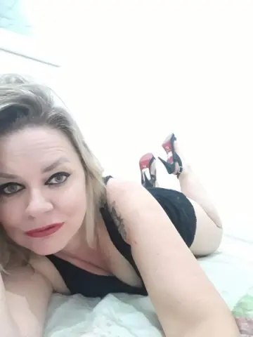 Blonde woman in a black tank top relaxing on a bed in a bright, minimalist room.