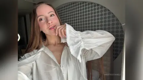 Young woman in a white linen blouse posing in a modern bedroom with a stylish patterned wall.