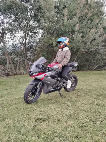 Adventurous motorcyclist in a brown jacket and helmet sitting on a red sportbike in a grassy forest setting.