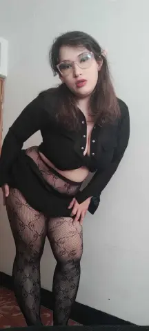 Woman in black long-sleeve top and patterned tights posing in a minimalist indoor setting.