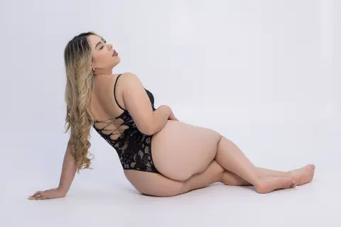 Curvy woman in black lace bodysuit posing elegantly on a white background.