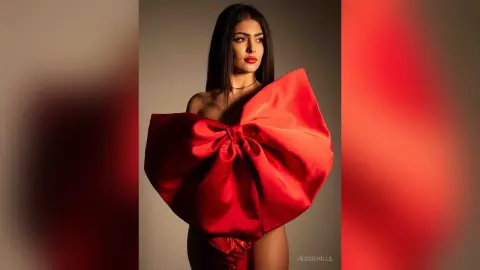 Elegant woman in a dramatic oversized red satin bow dress posing in a studio setting with a glamorous mood.