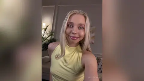 Smiling blonde woman in a yellow halter top posing in a cozy, brightly lit living room.