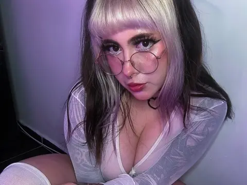 E-girl with blonde and purple hair wearing round glasses and a sheer white top in soft purple lighting.