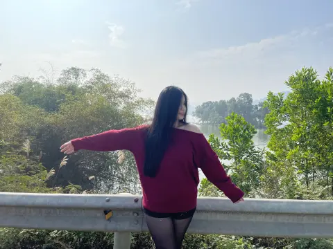 Woman in a burgundy long-sleeve top leaning on a guardrail overlooking a lush green lakeside landscape.