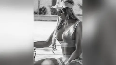 AndreaKalo wears a light-colored sports bra and visor, posing outdoors with her long hair down and a side profile view of her chest.