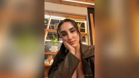 Young woman in a dark leather jacket posing with a thoughtful expression in a modern cafe setting.
