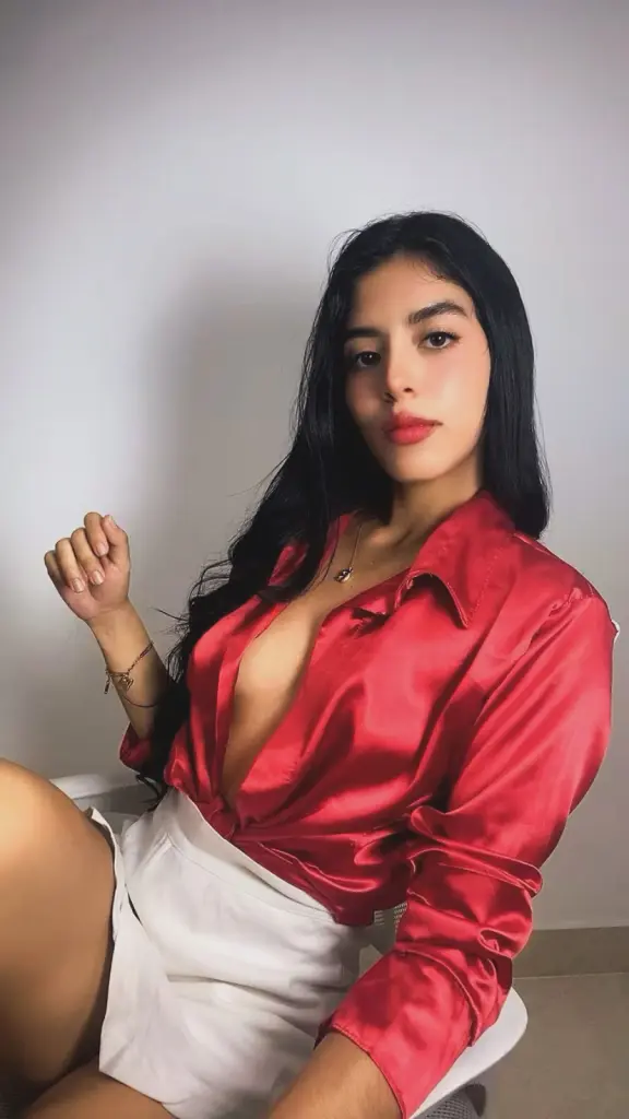 alanarouself poses in a black low-cut tank top and denim jeans, showing cleavage while sitting on a tan couch.