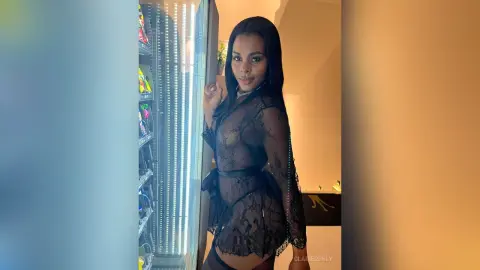 Elegant woman in a black lace sheer outfit posing confidently in a modern indoor setting.