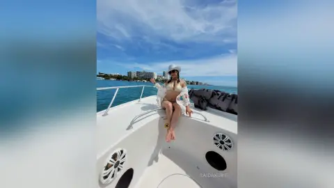 Woman in white bikini and sun hat relaxing on a white boat under a blue sky at sea.