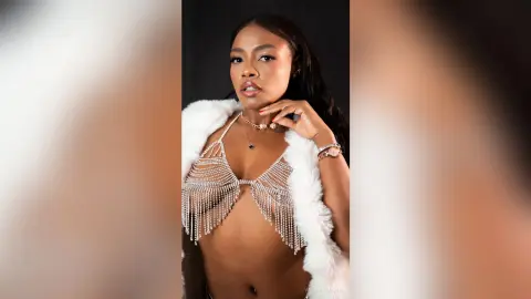 Glamorous woman in a silver beaded bikini top and white faux fur coat posing against a dark studio background.