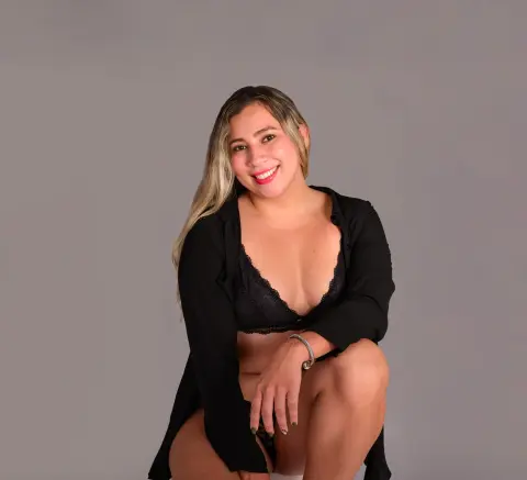 Smiling woman in a black lace bra and open shirt posing against a gray studio background.