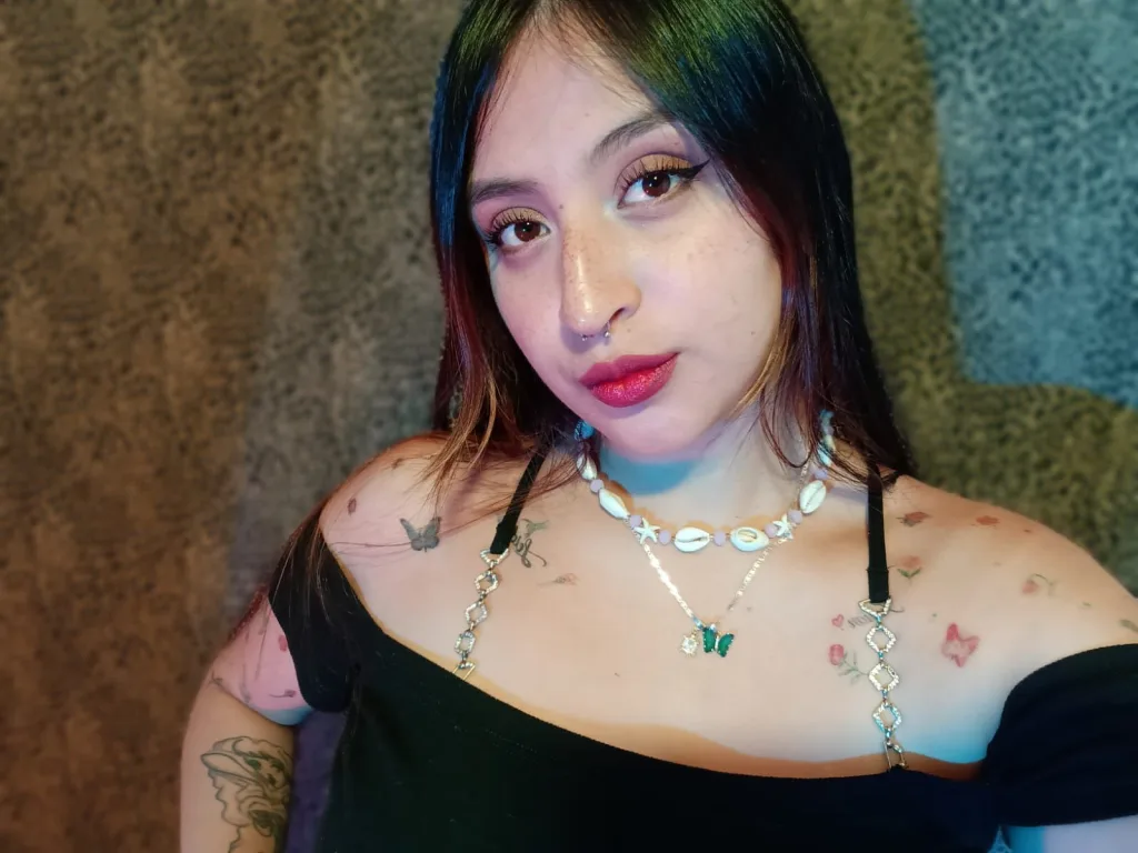 Gabbycooper poses with her arms crossed, showing her bare shoulders and cleavage while looking at the camera with long dark hair.