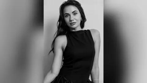 Elegant woman in a black sleeveless dress posing for a sophisticated black and white portrait.