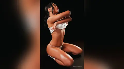 Young woman in white bikini posing confidently against a dark studio background.