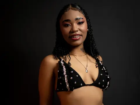 Smiling young woman with braided hair wearing a black sequined bikini top against a dark studio background.