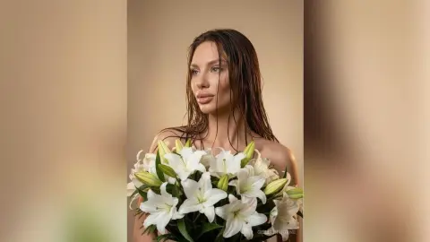 Beautiful woman with wet hair holding a bouquet of white lilies in a soft, moody studio setting.