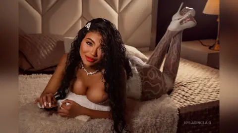 Smiling woman in white lace lingerie and patterned tights lounging on a cozy bed in a warm, romantic mood.