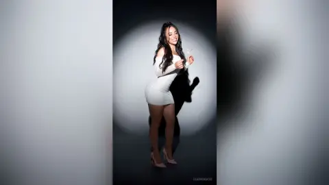 Smiling woman in a white cocktail dress posing in a studio setting with dramatic lighting.