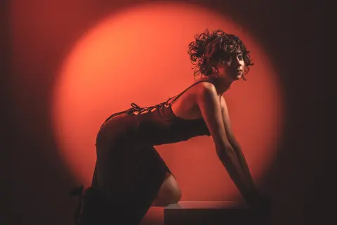 Moody portrait of a woman in a black dress posing against a warm red spotlight background.