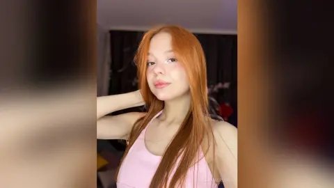 Redheaded woman in a pink tank top smiling in a cozy indoor setting.