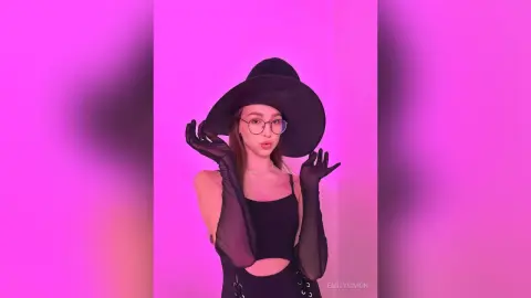 Stylish woman in a black tank top and wide-brimmed hat posing against a vibrant pink background.