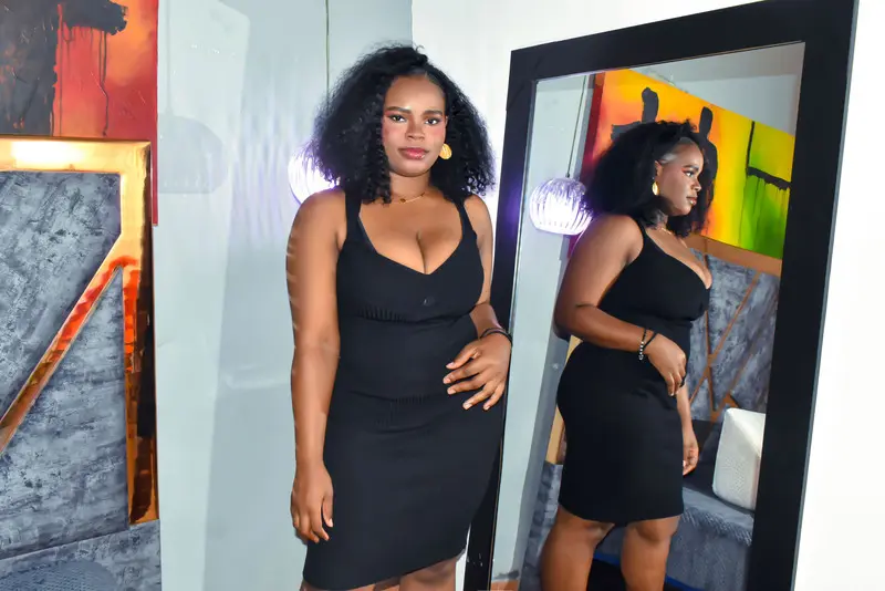 SkyllerFoxy — Curvy woman in a chic black midi dress posing in front of a mirror in a modern, stylish room.