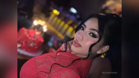 Glamorous woman in a red lace dress posing with elegant makeup in a dimly lit evening setting.