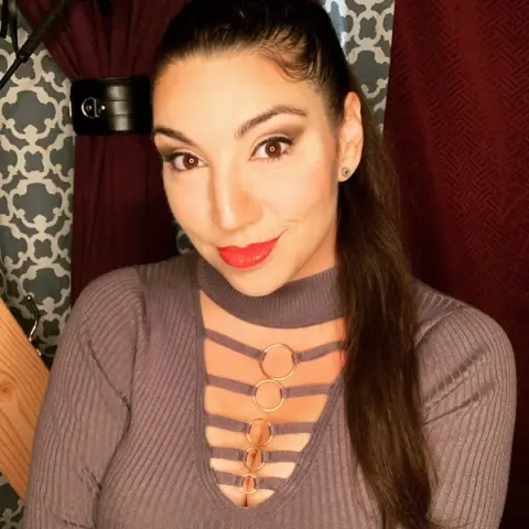 Smiling woman in a mauve ribbed cutout top posing indoors with a warm, stylish mood.