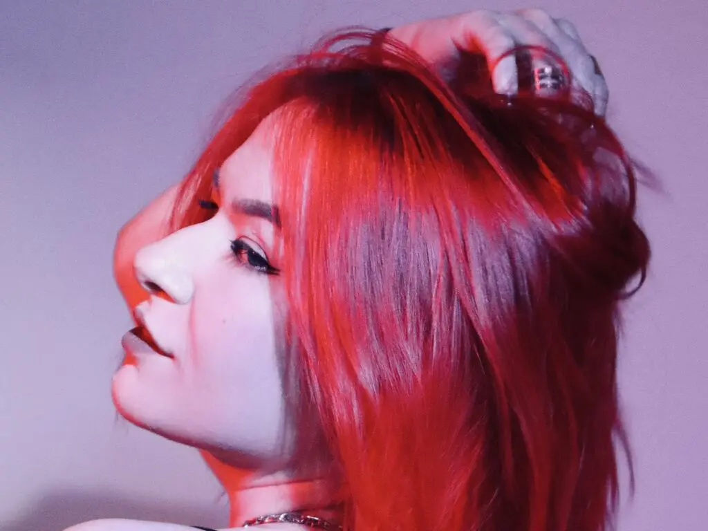 Side profile of a woman with long red hair posing under moody pink and red neon lighting.