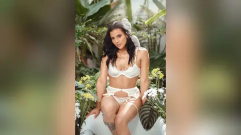 Beautiful woman in white lace lingerie relaxing in a lush tropical garden setting.