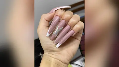 Close-up of long almond-shaped nude manicure with white French tips and sparkling rhinestone star accents.