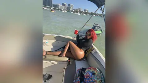 Stylish woman in a black bodysuit relaxing on a boat on a sunny day by the city waterfront.