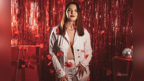 Young woman in a white blazer posing against a festive red tinsel backdrop for a glamorous party mood.