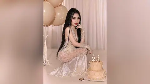 Elegant woman in a white lace gown celebrating her 23rd birthday with gold balloons and a tiered cake.