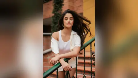 TefyRusso poses outdoors on a balcony with her long dark hair blowing, wearing a white tank top and matching white shorts.