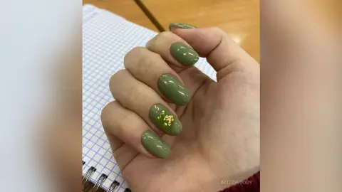 Close-up of a hand with olive green manicured nails featuring gold glitter accents on a notebook background.