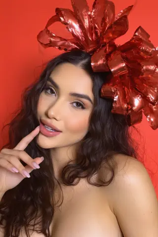 Glamorous woman with wavy hair wearing a large metallic red bow against a vibrant red background.